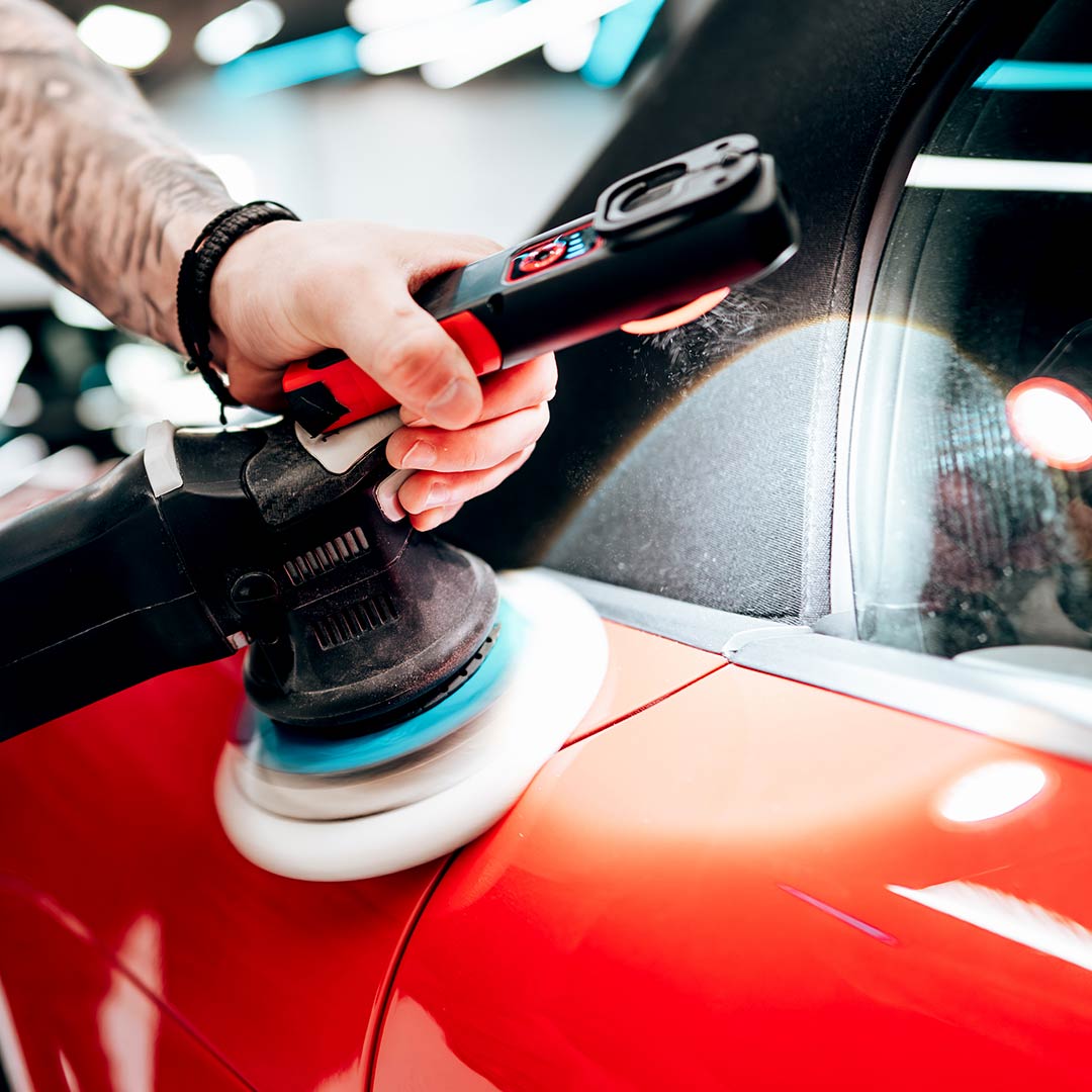 man applying wax to red vehicle