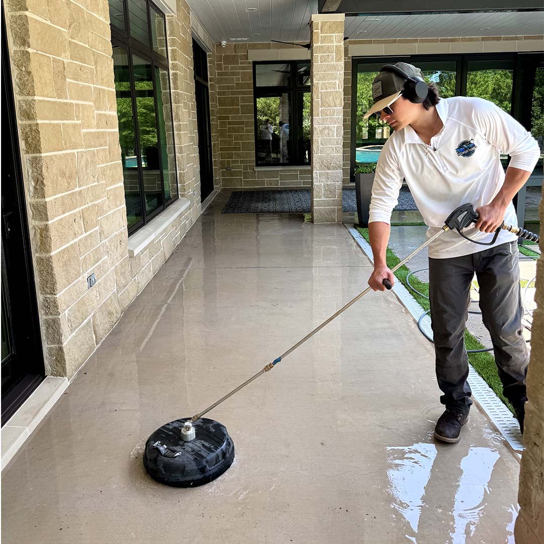 man pressure washing concrete walkway in backyard