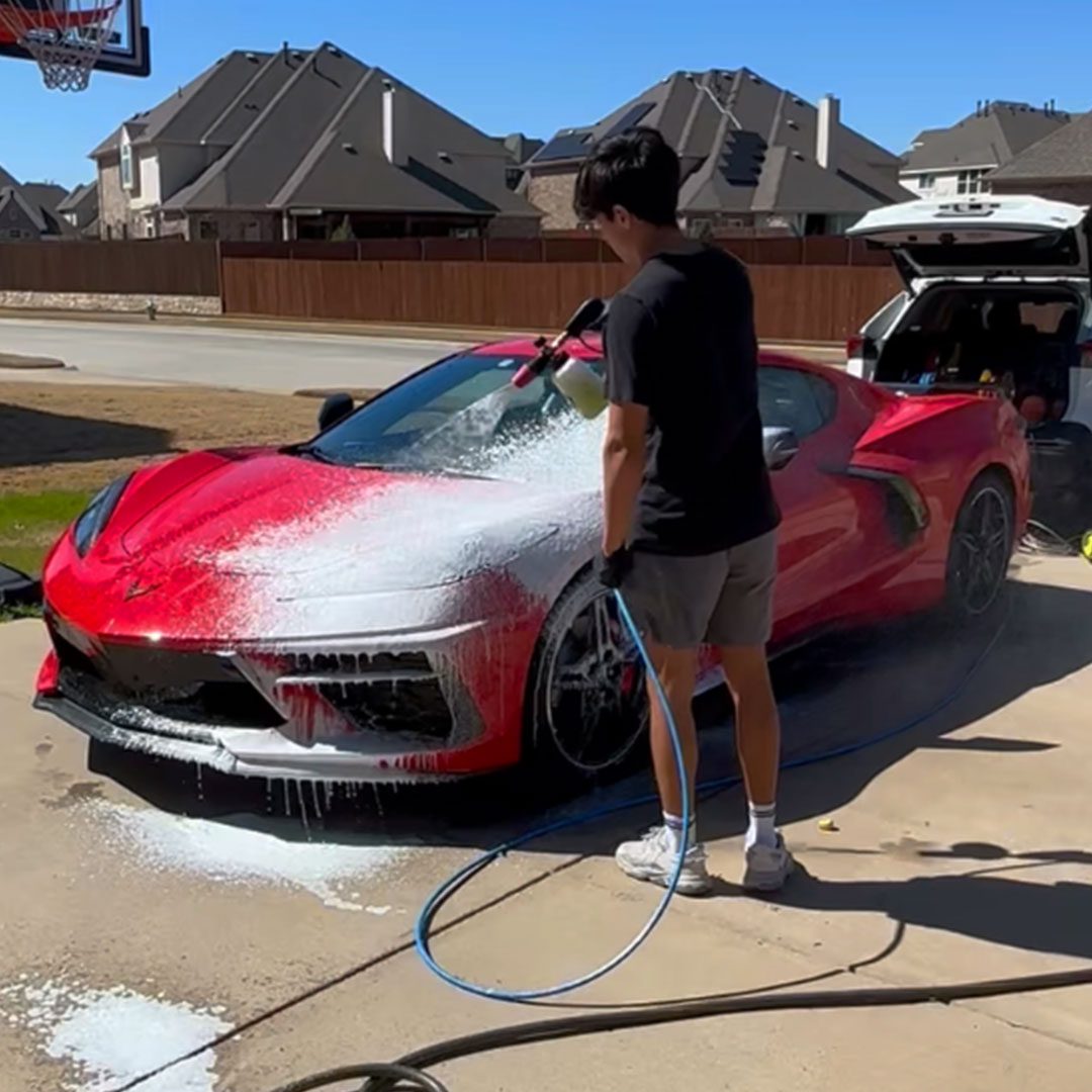 Man spray soap on red corvette in driveway