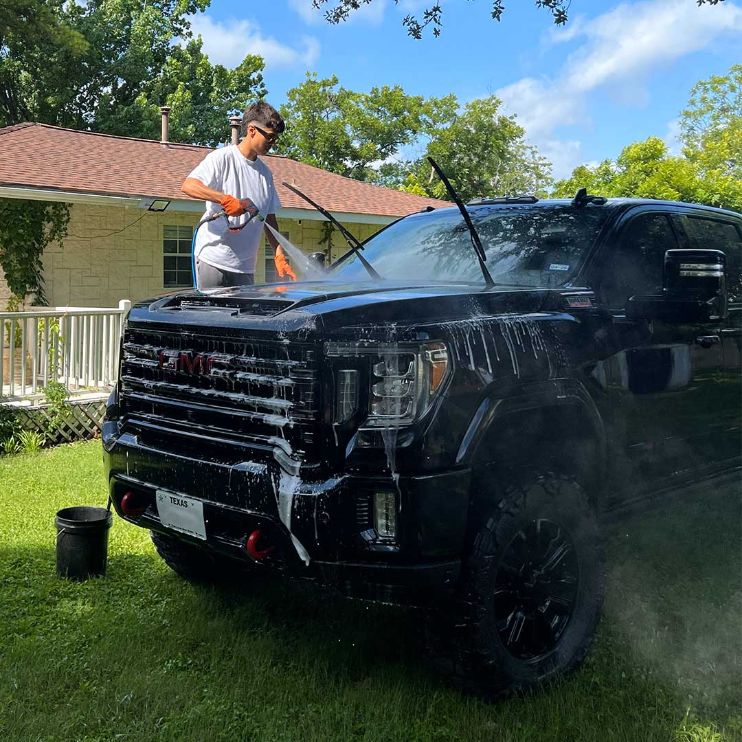 man washing black GMC truck with power sprayer