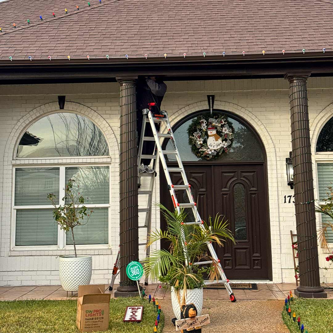 Technician installing custom Christmas lights on the roofline and columns of a residential home in Dallas-Fort Worth, TX